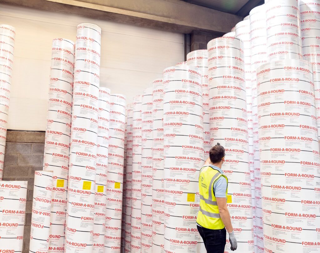 A factory worker with cardboard column moulds towering above him