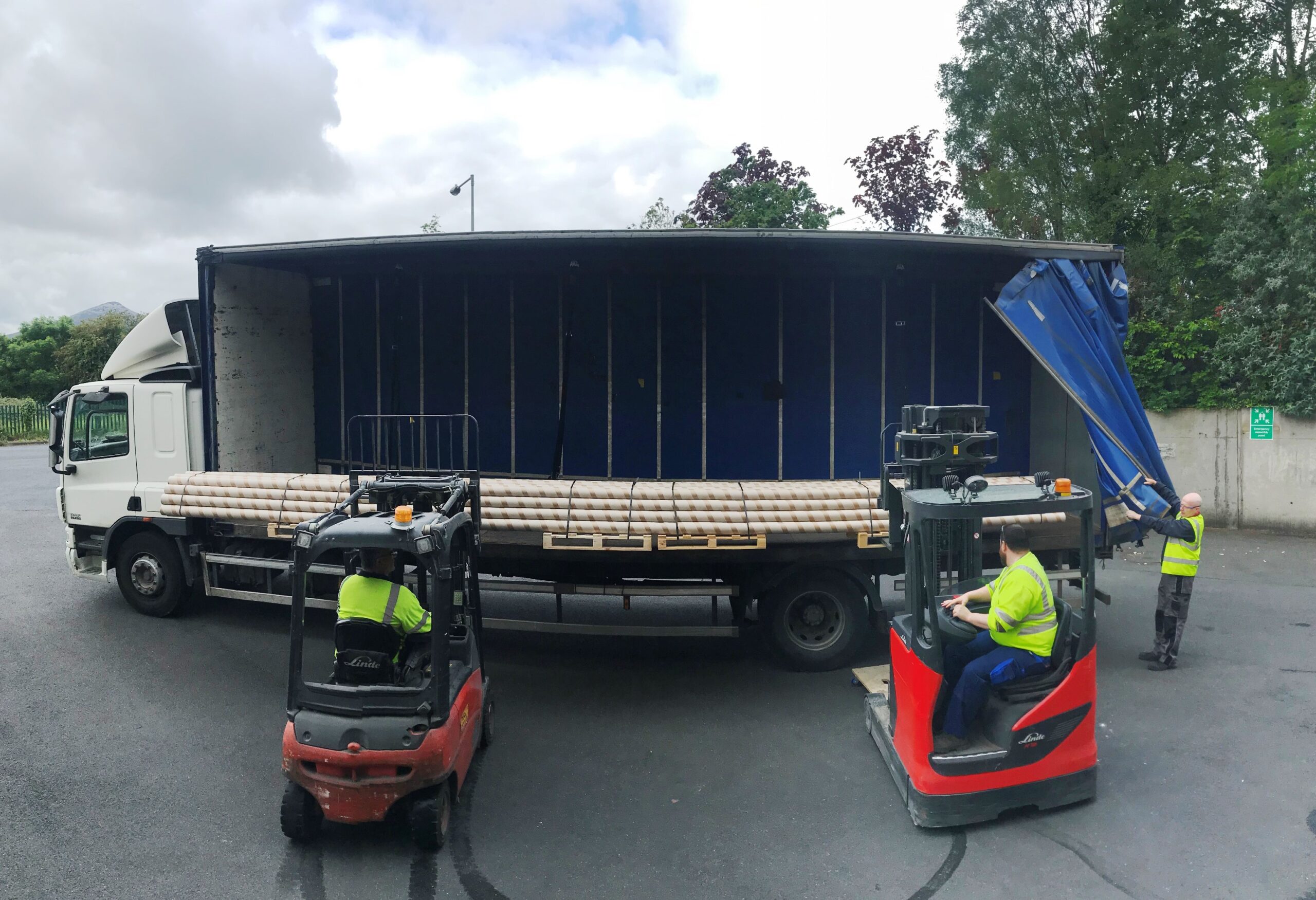 Extra long cardboard tubes being loaded by two forklifts onto a truck